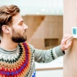 Man adjusting temperature with thermostat at home